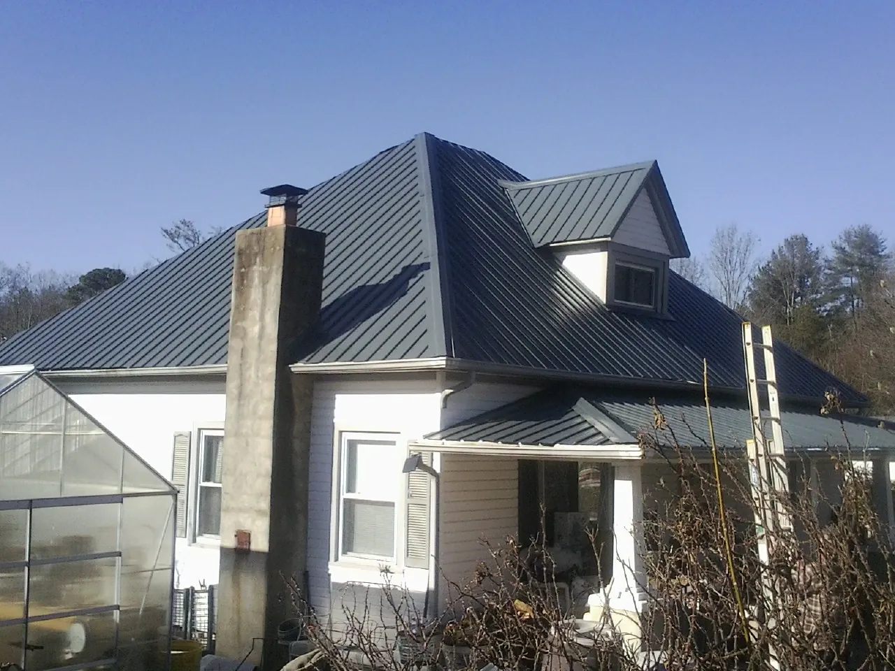 Dark blue standing seam metal roof on a white farmhouse with dormer — Slate & Tile Roof Repair by Roofing Brothers in Wharton