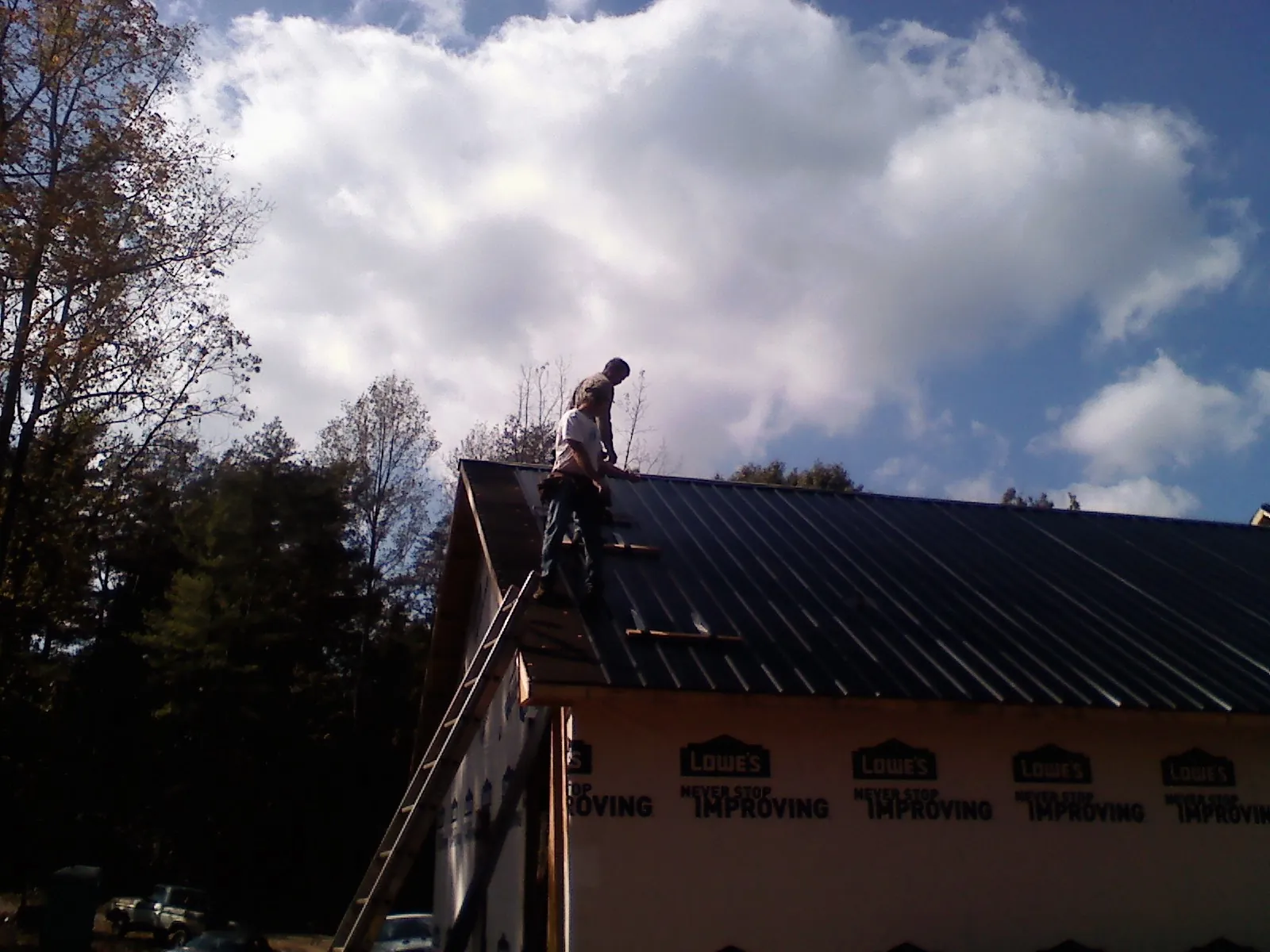Roofer fastening dark metal panels high against a cloudy sky, from a Roof Inspection job in Wharton