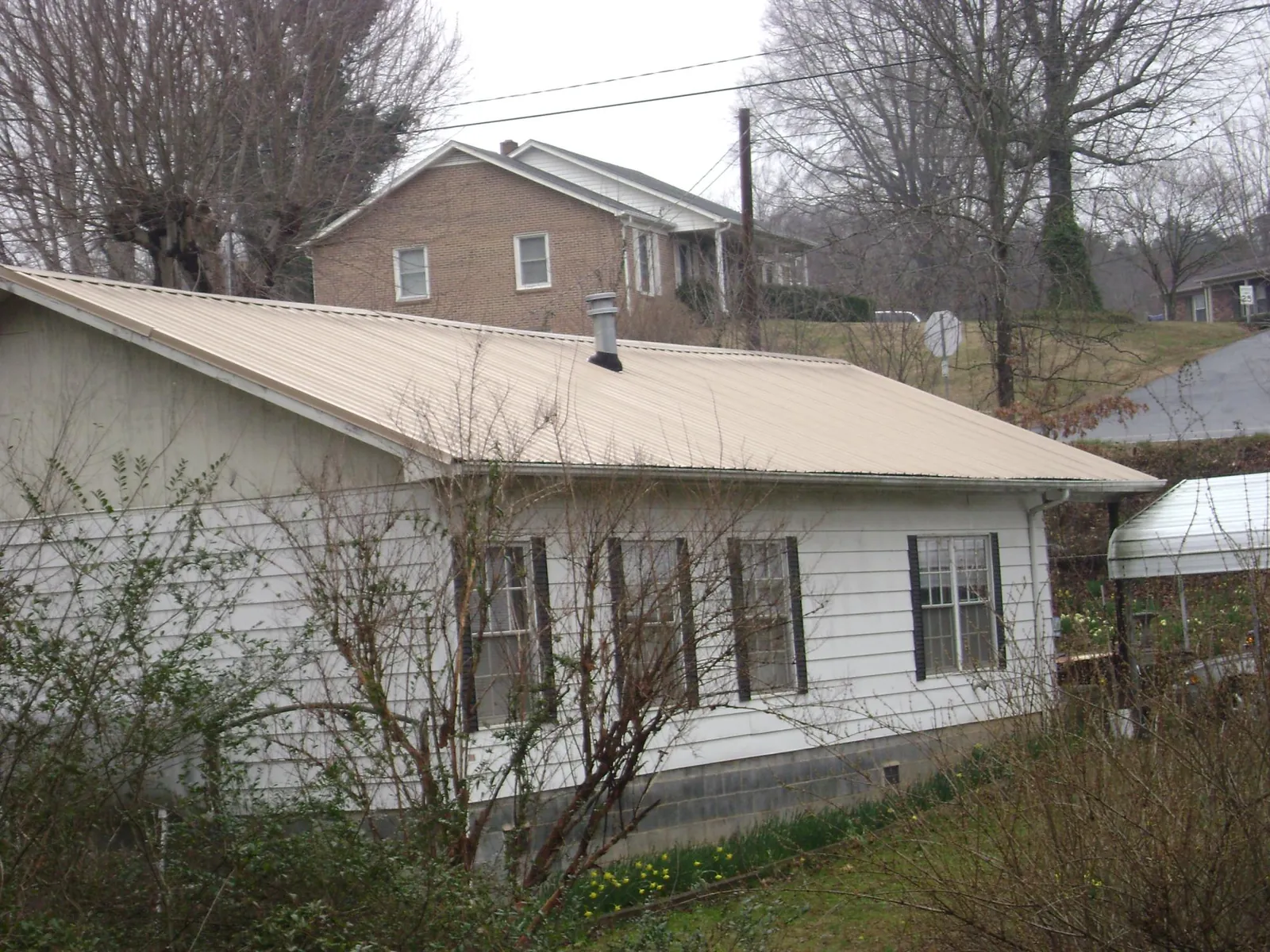Tan metal roof on a white sided house set into a hillside — Commercial Roofing by Roofing Brothers in Wharton